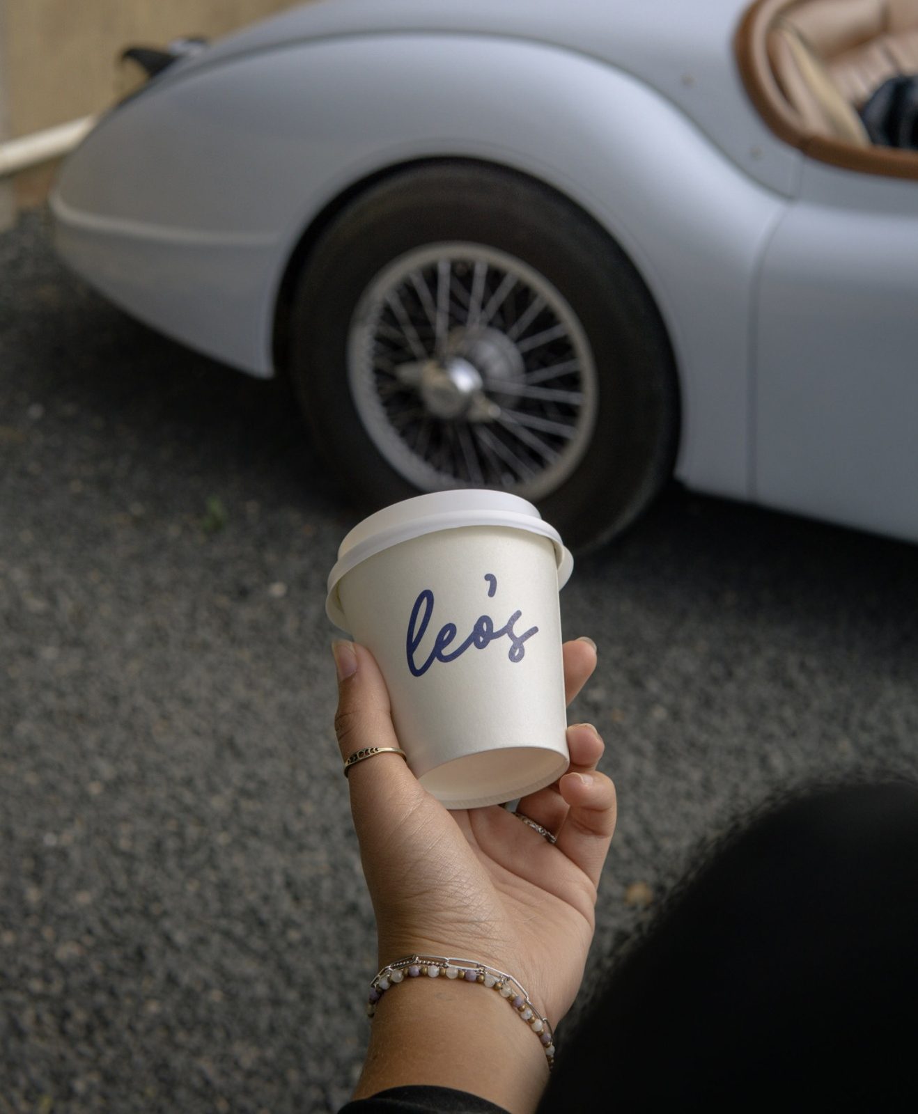 A Leo's takeaway cup held beside a classic car